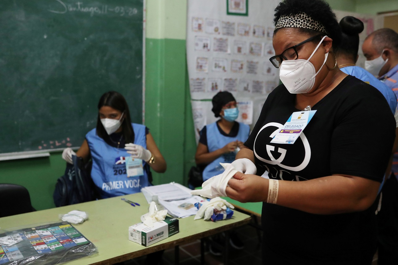 An electoral worker wearing a face mask puts on protective gloves during the COVID-19 outbreak in Santiago, Dominican Republic, July 5, 2020. 