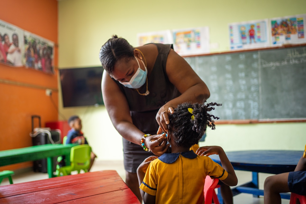A teacher helps a student put on her face mask during class at the New Edition School in Kasoa, Ghana, on July 4, 2022. 