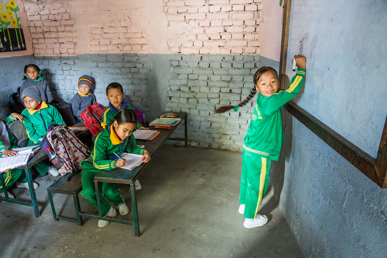 In a classroom in rural Nepal, a young girl writes on a chalkboard.