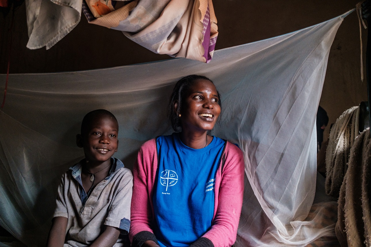 A mother and her son sit beside their bedroom’s malaria prevention net in Buyende, Uganda.