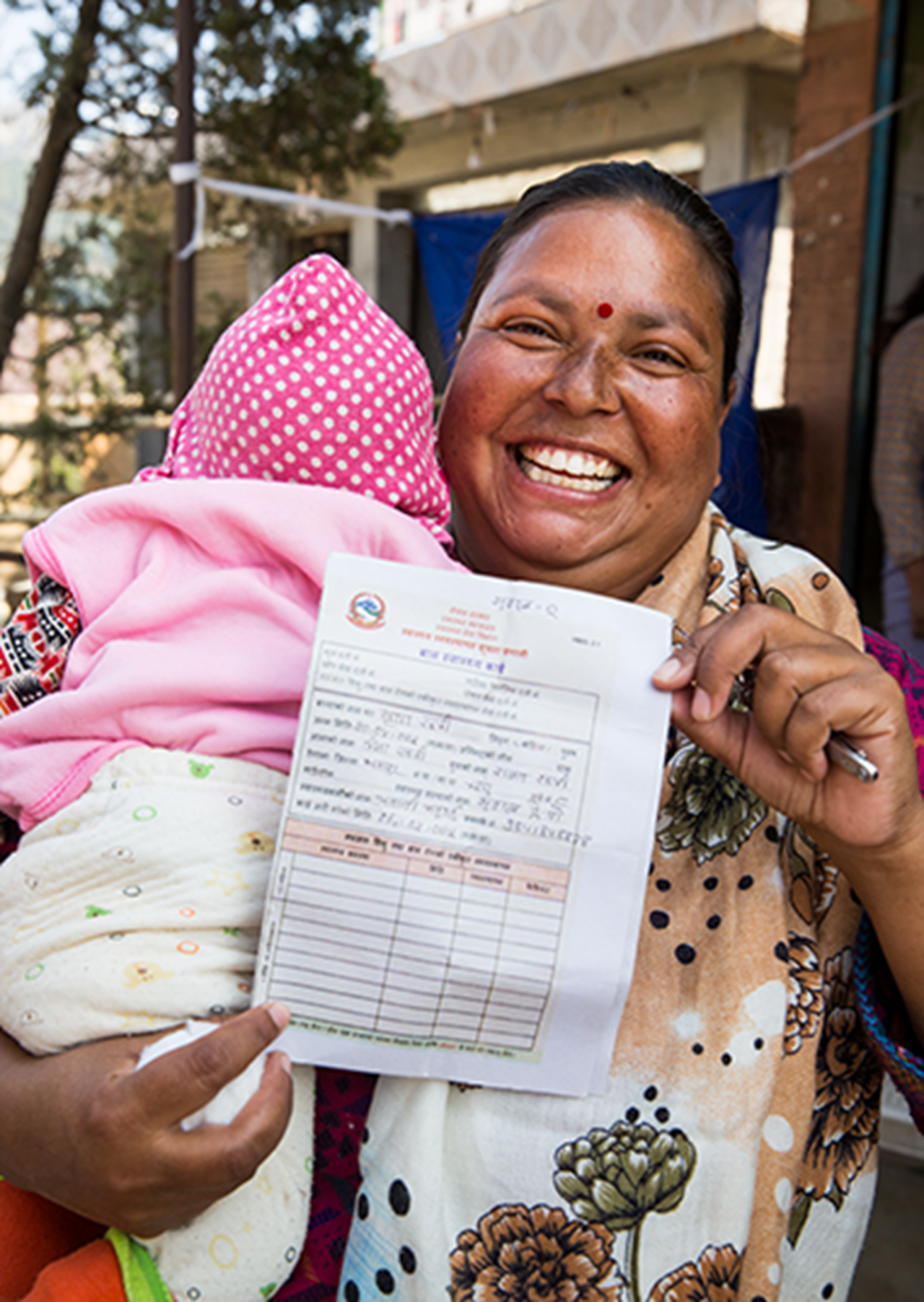 A mother displays her three-month-old's vaccination card outside of an outreach clinic in Bhaktapur, Nepal.